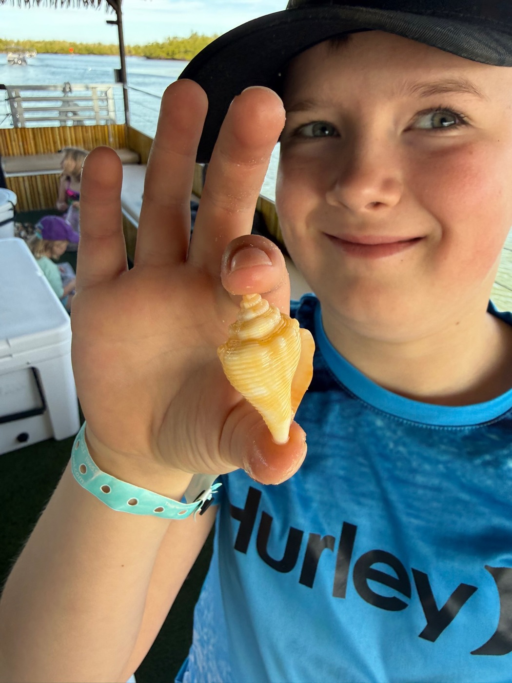 Boy holding a banded tulip shell on the tiki boat during a shelling tour