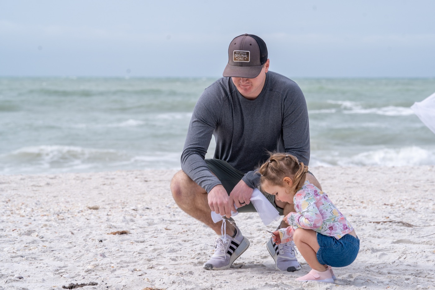 Dad and toddler kneeling on the beach picking up shells together