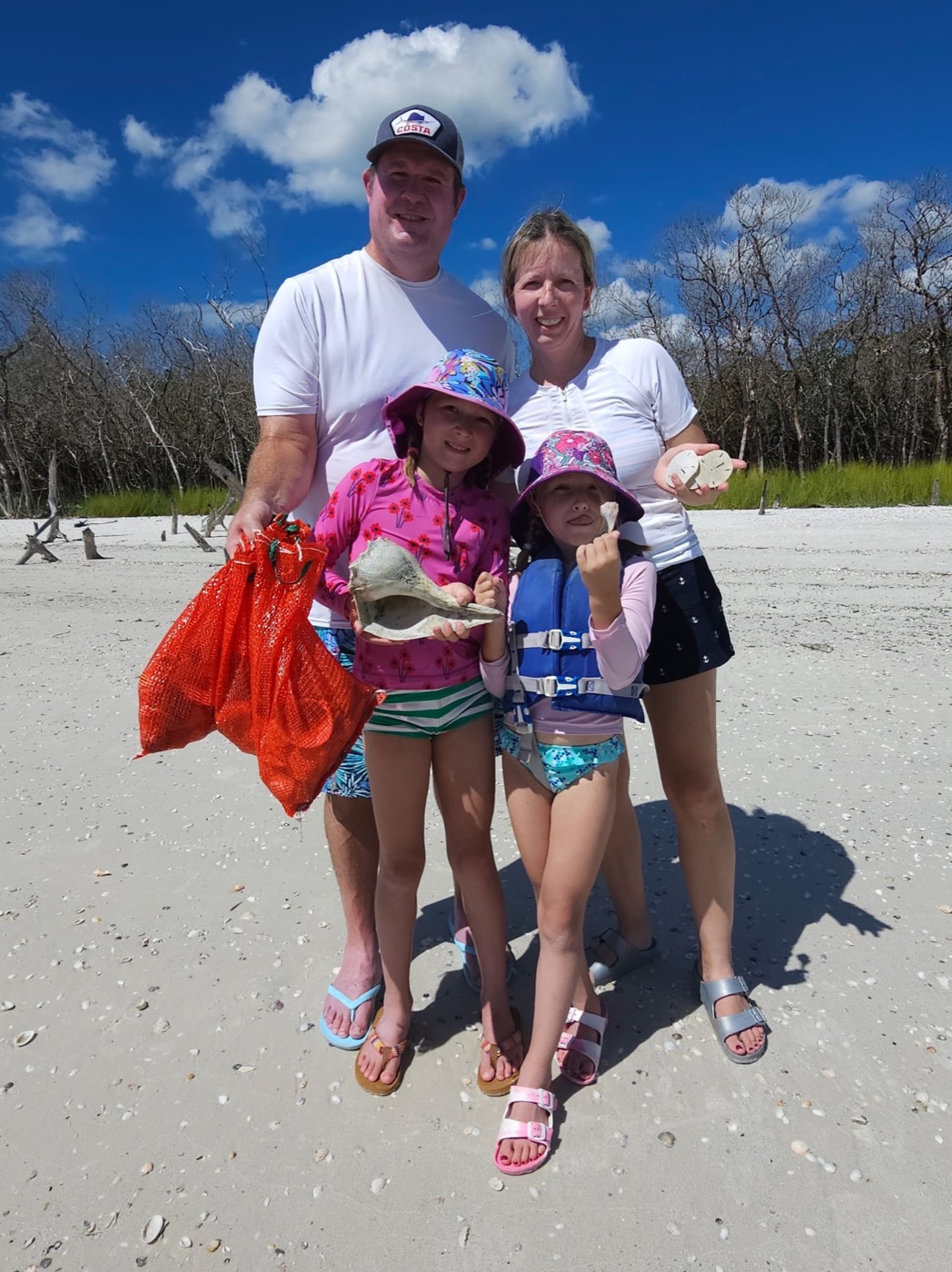 Family of girls holding shells by driftwood on a sunny day