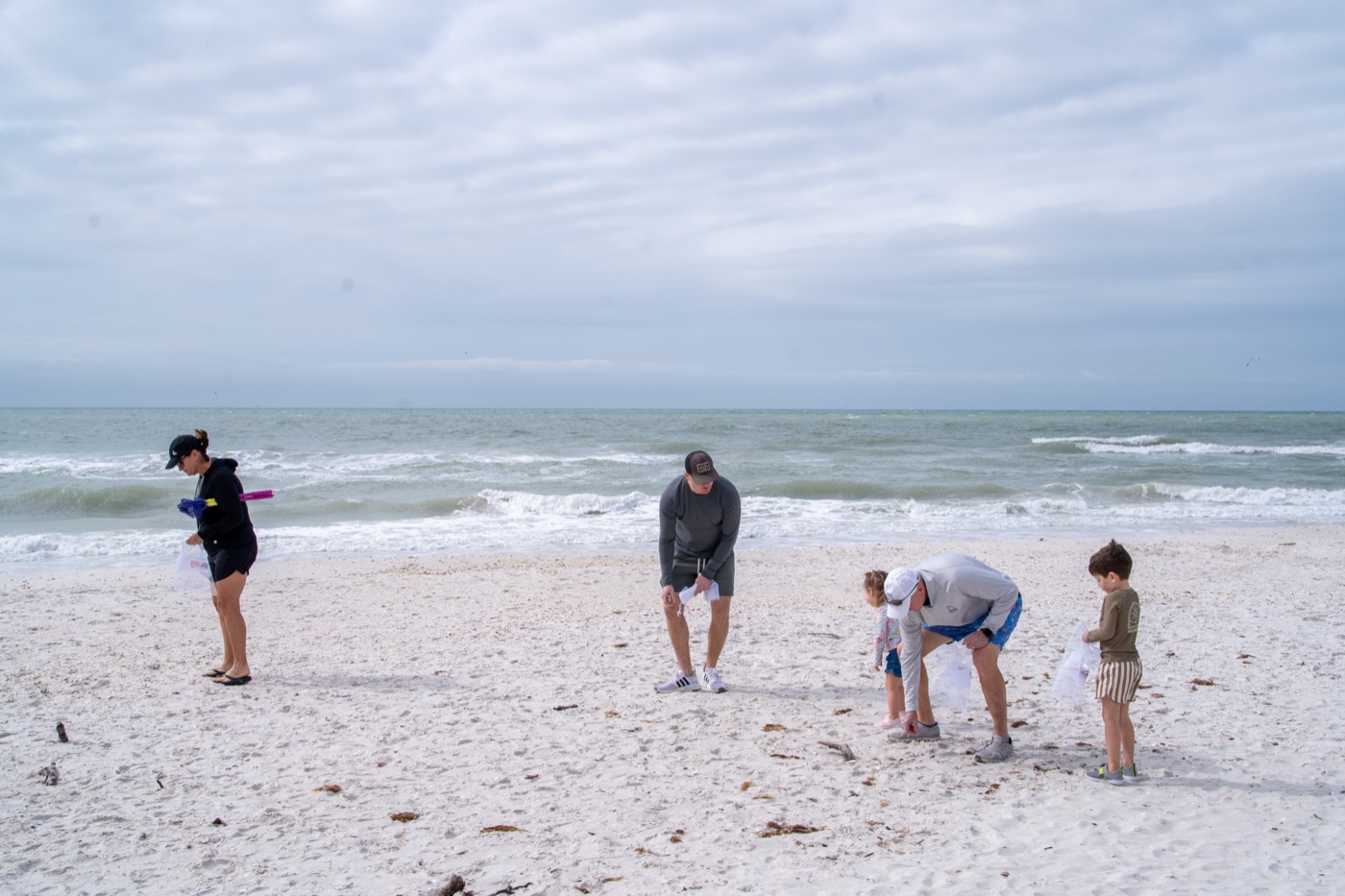Father and son bending down to collect shells in a mesh bag
