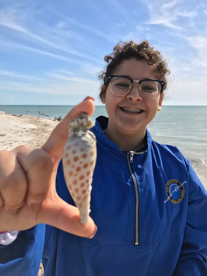 A smiling girl holding up the spotted Junonia shell she found