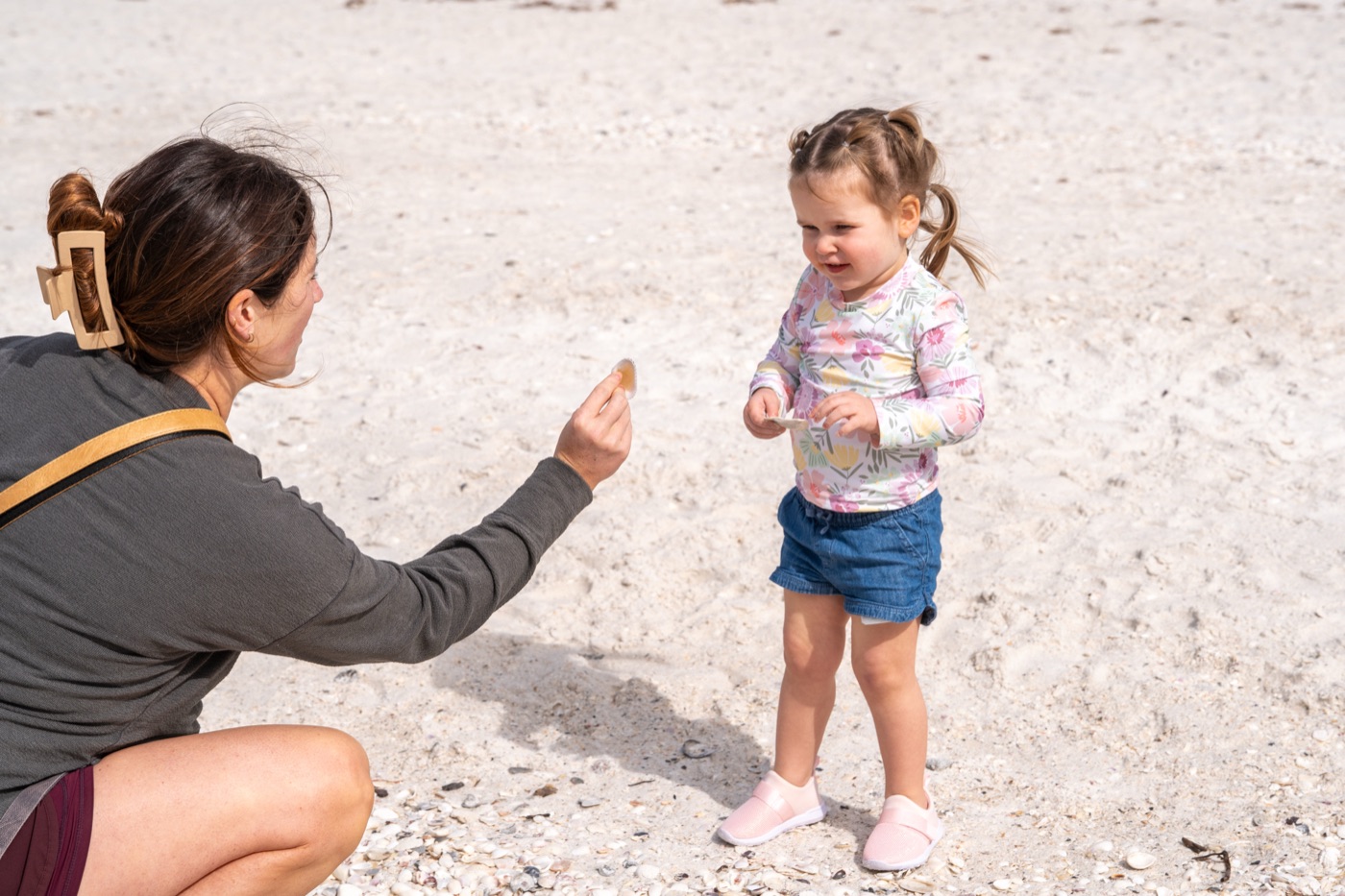 Mother and laughing toddler examining a shell on the beach